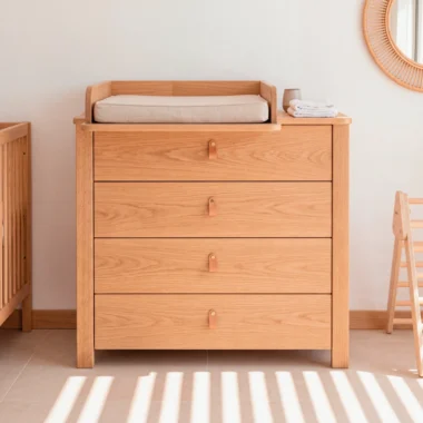 Cómoda cambiador Halvor en madera de roble con manijas de cuero, junto a cuna en cuarto de bebé